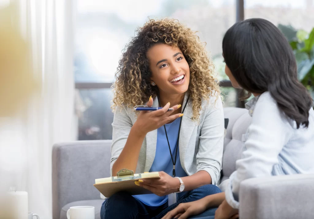 Smiling woman with curly hair talking while holding a clipboard.
